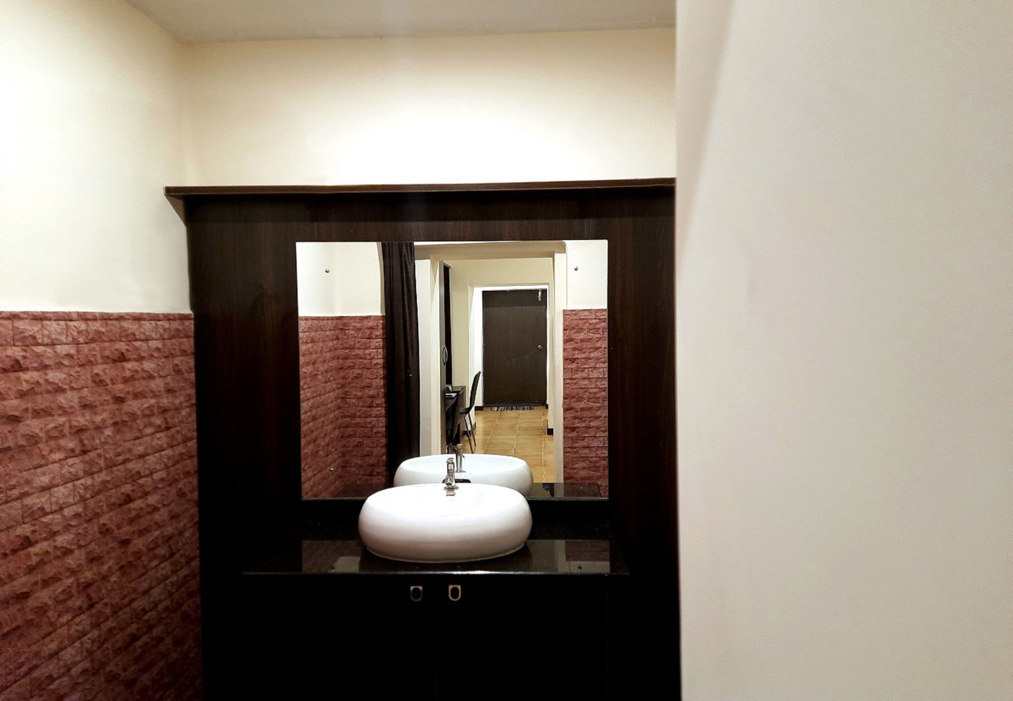 A bathroom with a white sink, dark wooden vanity, and a mirror reflecting a door and a tiled floor.