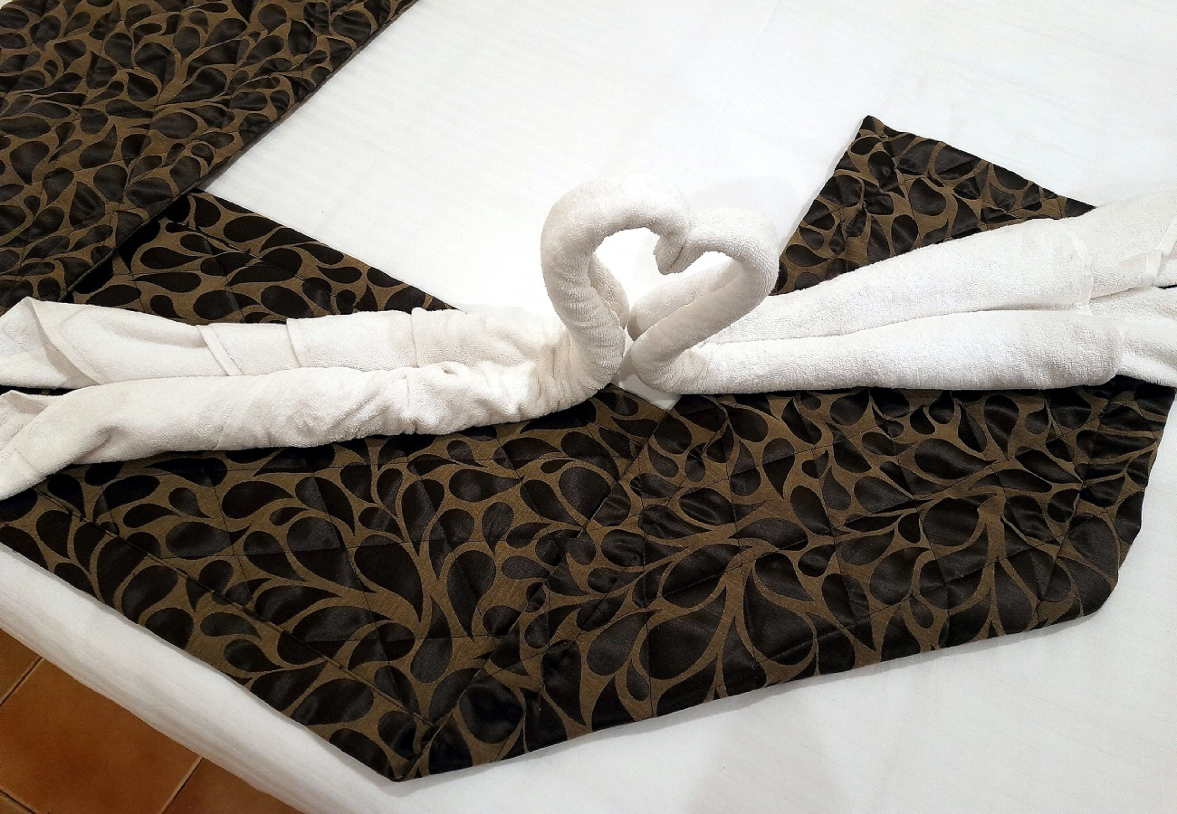 Uma cama com colcha estampada, arranjo de toalhas em formato de coração e travesseiro branco.