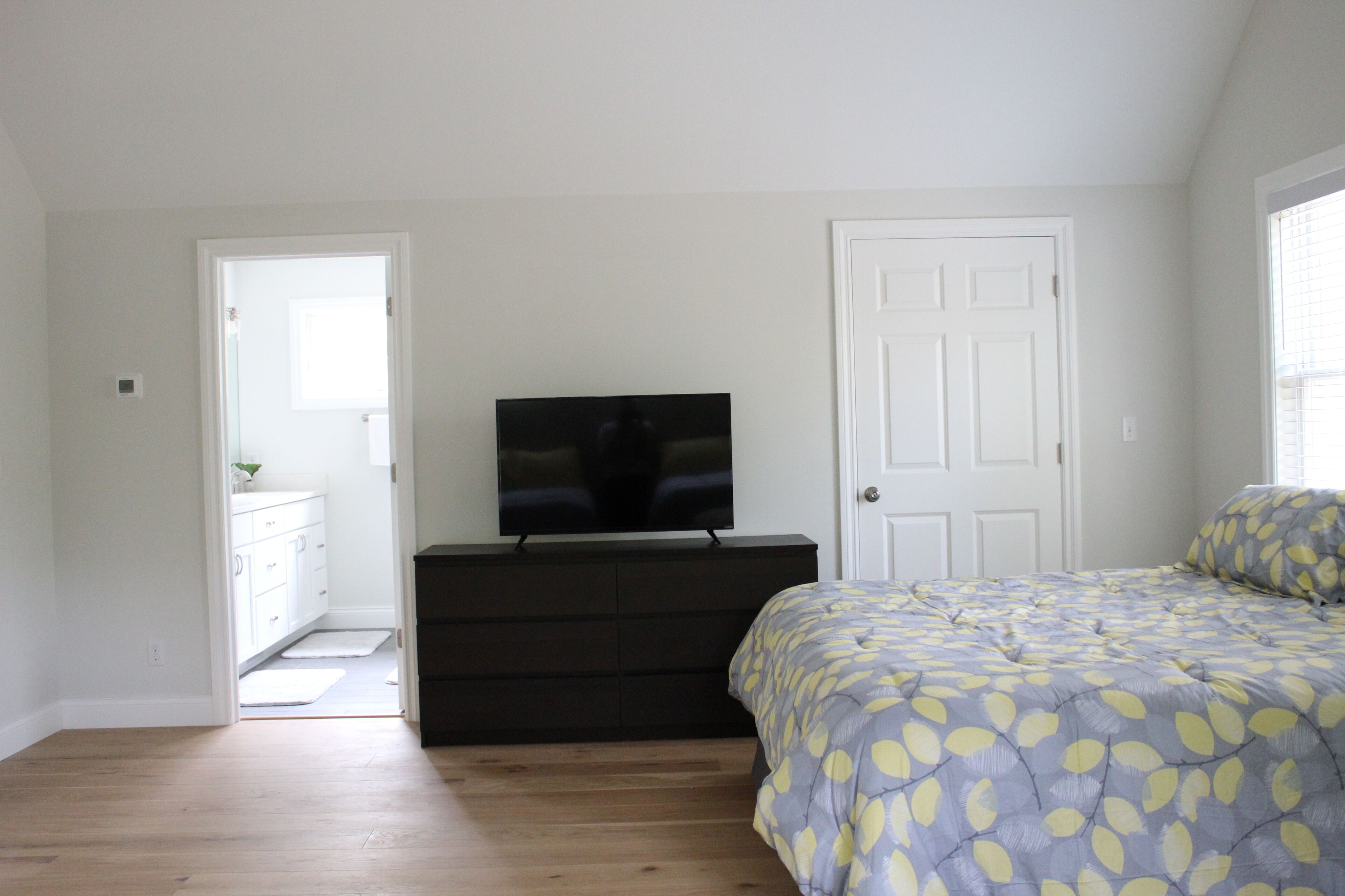 Une chambre à coucher avec un lit, une commode, un téléviseur et une porte.