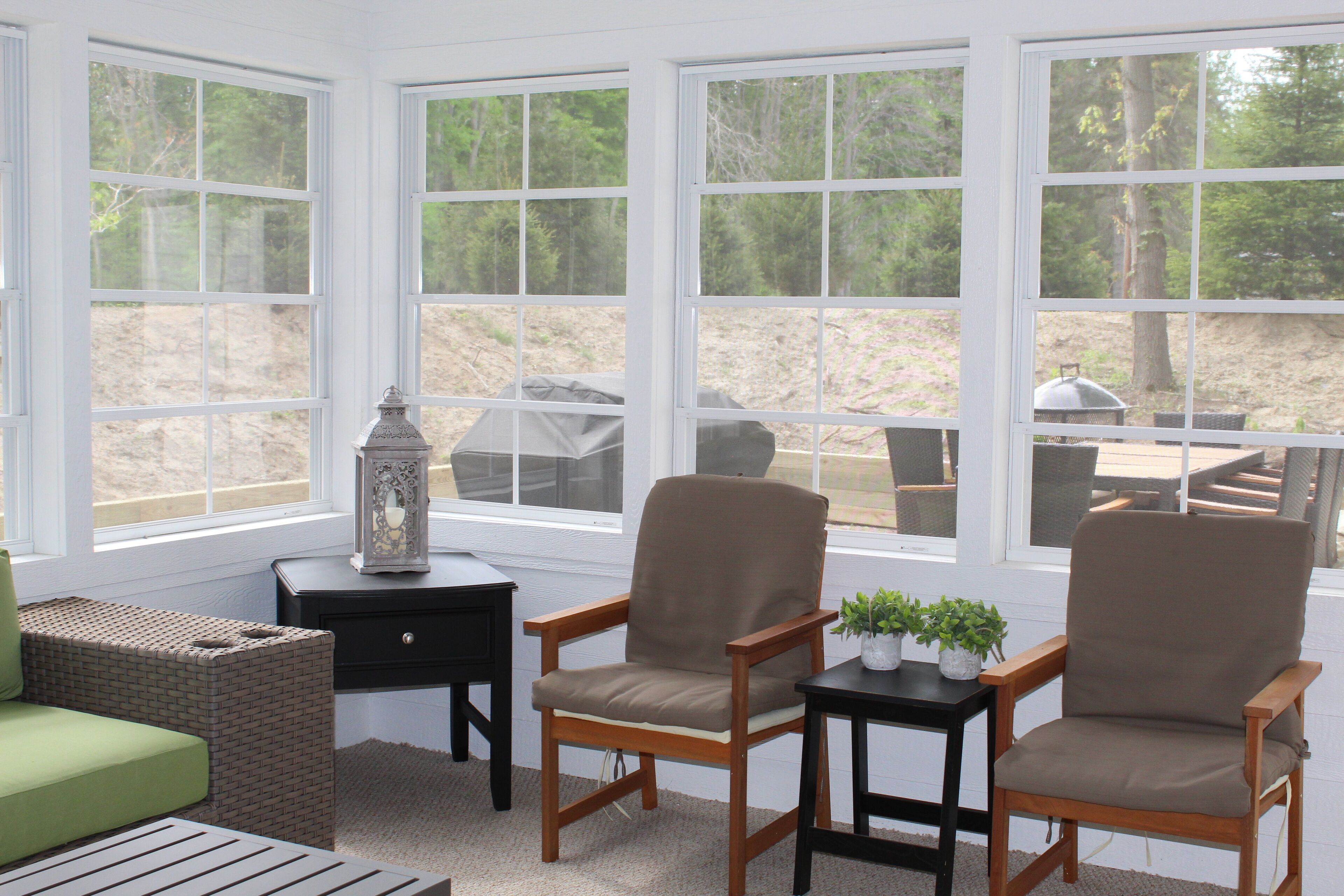 A sunroom with large windows, two wooden chairs, a small table, and a decorative lantern.