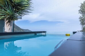 Una piscina azul cristalina con vistas al océano y montañas al fondo.