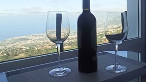 Een fles wijn en twee glaasjes op een tafel bij een raam met uitzicht op een stadsbeeld.