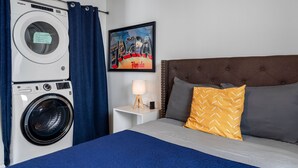 A hotel room with a bed, a nightstand with a lamp, a washing machine, and a framed picture on the wall. - 【3 Bedrooms/Firepit/Private Outdoor Dining Area /Local History Themed/Sleep... (Tampa)