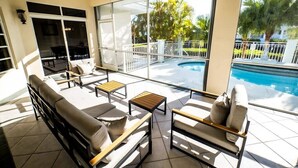 A sunlit outdoor lounge area with a pool, featuring a sofa, chairs, and a small table. - *Newly Renovated Single Family Home w/Private Pool (Key Colony Beach)