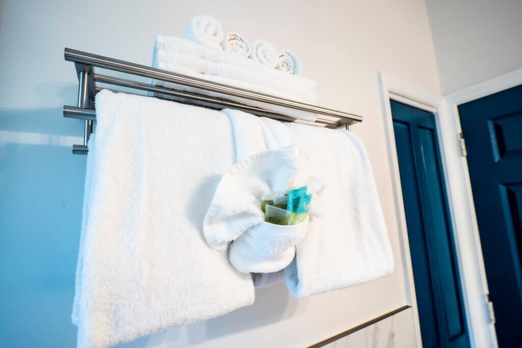 A bathroom with a towel rack holding several white towels and a folded towel with toiletries.