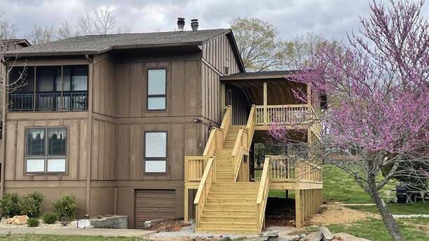 A two-story building with a wooden staircase leading to a balcony. - Welcome to On the Green – Your Golfing Getaway (Bronston)