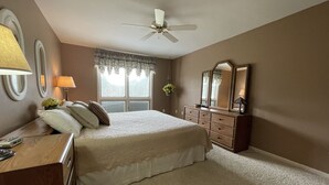 A bedroom with a bed, dresser, mirror, ceiling fan, and window with curtains. - Welcome to On the Green – Your Golfing Getaway (Bronston)
