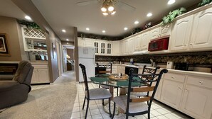 A modern kitchen with white cabinets, a dining area with a glass table and chairs, and a ceiling fan. - Welcome to On the Green – Your Golfing Getaway (Bronston)