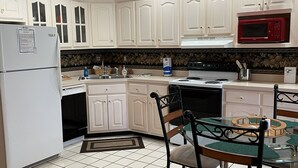A kitchen with white cabinets, a red microwave, a stove, and a dining area with a glass table and chairs. - Welcome to On the Green – Your Golfing Getaway (Bronston)
