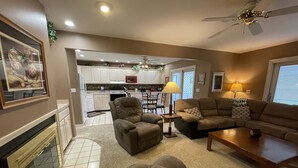 A living room with a fireplace, a sofa set, a coffee table, and a dining area with a chandelier. - Welcome to On the Green – Your Golfing Getaway (Bronston)