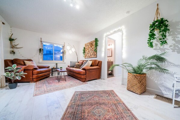 A living room with two leather sofas, a coffee table, a large window, and various plants.