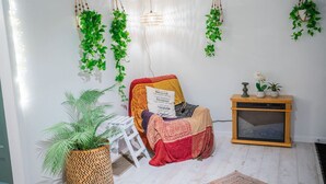 Una habitación acogedora con un banco de madera, una mesita con adornos, plantas colgantes y una cesta tejida con una planta.
