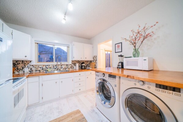 Une cuisine compacte avec des meubles blancs, un lave-linge, un four à micro-ondes et un petit évier.