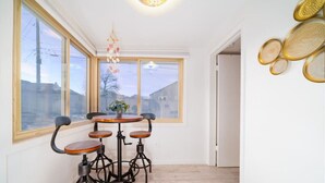 Un comedor con una mesa redonda y cuatro sillas, una lámpara colgante y vistas amplias a través de ventanas grandes.