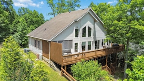 A two-story house with a wooden deck and a large window overlooking a lush green landscape. - Welcome to “Hillside Haven” – The Perfect Family and Friends Vacation Spot (Burnside)