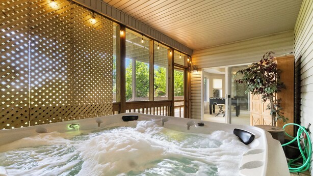 A hot tub with a wooden deck and a glass partition. - Welcome to “Hillside Haven” – The Perfect Family and Friends Vacation Spot (Burnside)
