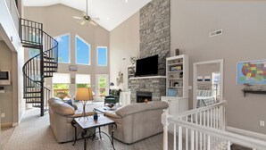 A spacious living room with a fireplace, a stone accent wall, a large TV, and a spiral staircase. - Welcome to “Hillside Haven”  – The Perfect Family and Friends Vacation Spot (Burnside)