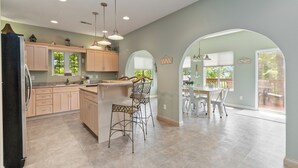A spacious kitchen with light-colored cabinets, a central island with bar stools, and a dining area with a large window. - Welcome to “Hillside Haven” – The Perfect Family and Friends Vacation Spot (Burnside)