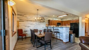Eine moderne Küche mit Holzschränken, einem Essbereich mit Holztisch und -stühlen sowie einer integrierten Kücheninsel mit Kühlschrank und Mikrowelle.