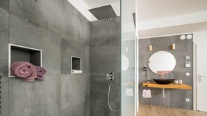 A modern bathroom with a glass-enclosed shower, a wooden vanity with a round mirror, and a towel rack with folded towels. - Prime Loft, Prime Loft near Naschmarkt (Vienna)