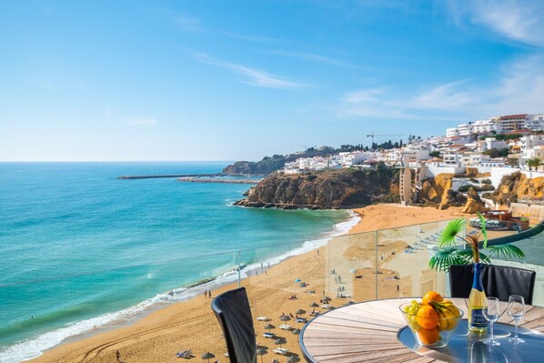 Une vue sur la mer, avec une table sur le balcon, un panier de fruits et une bouteille de vin.