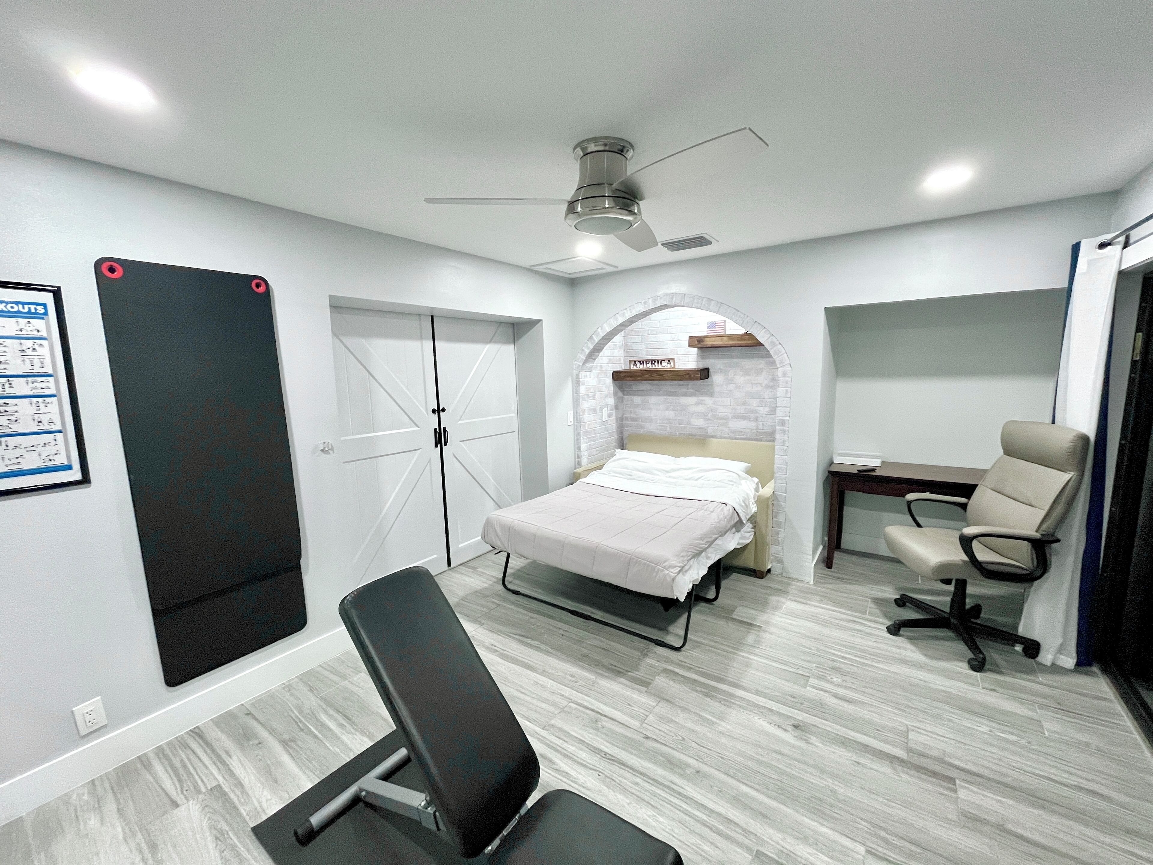 A bedroom with a bed, a desk, a chair, a wardrobe, and a ceiling fan.
