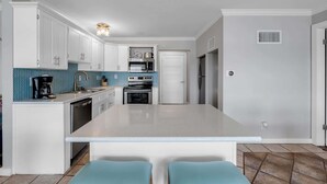 Een moderne keuken met witte kasten, een centraal eiland en een blauwe betegelde achterwand.