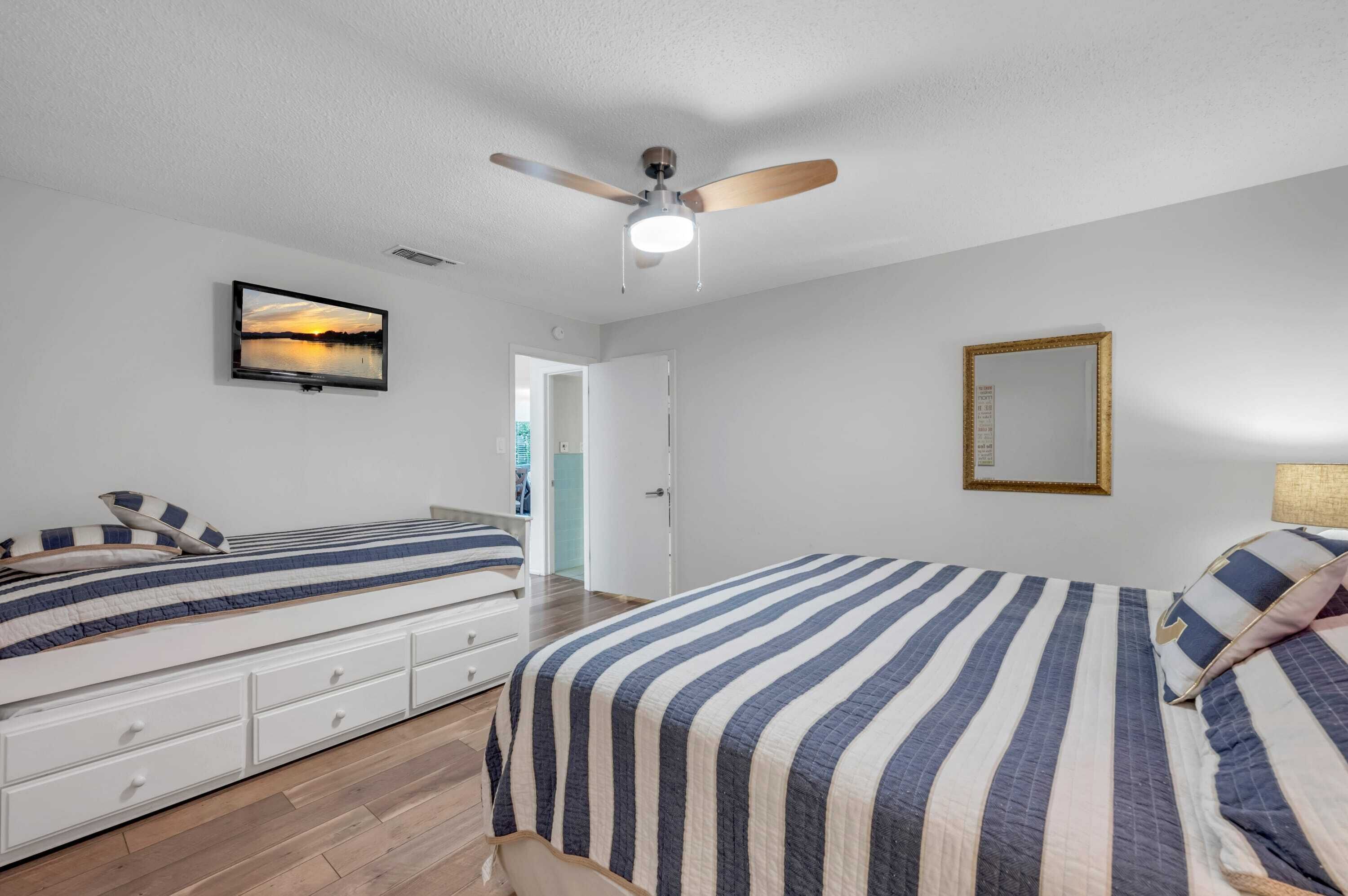 A bedroom with two beds, a ceiling fan, a framed picture, and a door leading to another room.