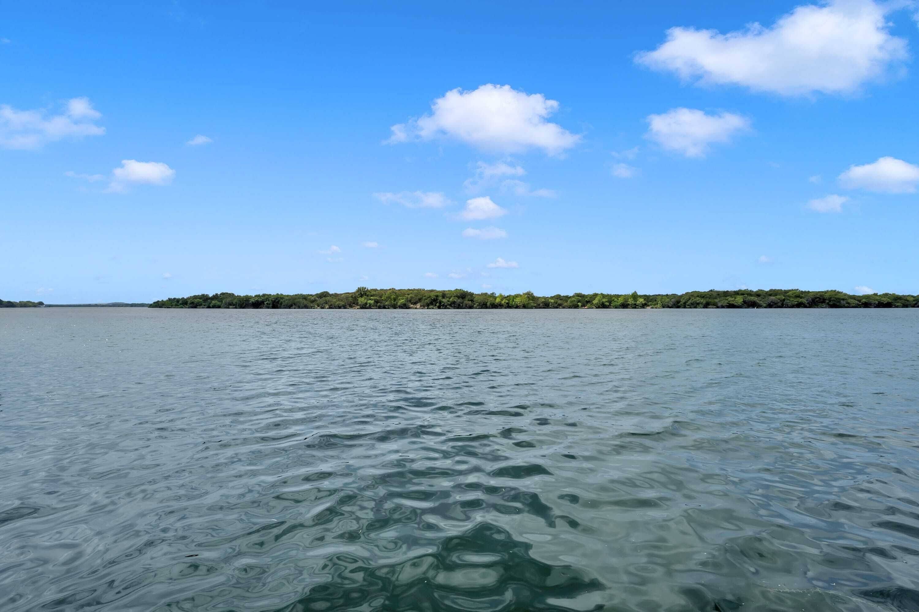 Ruhige Wasserfläche mit einer grünen Landmasse in der Ferne unter blauem Himmel.