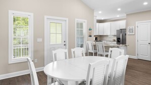 A spacious kitchen with white cabinets, a central island, and a dining area with a round table and white chairs.