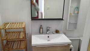 A bathroom with a wooden shelf, a white sink, a mirror, and a medicine cabinet. - En Ville Avec un air de Campagne (Arles)