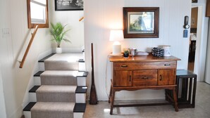 A staircase with a wooden handrail, a potted plant, and a lamp on a wooden console table. - Lake House with gorgeous view, private beach, dock space, fireplace, hammock (Bolton Landing)
