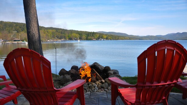 Two red Adirondack chairs facing a lake with a fire pit between them. - Lake House with gorgeous view, private beach, dock space, fireplace, hammock (Bolton Landing)