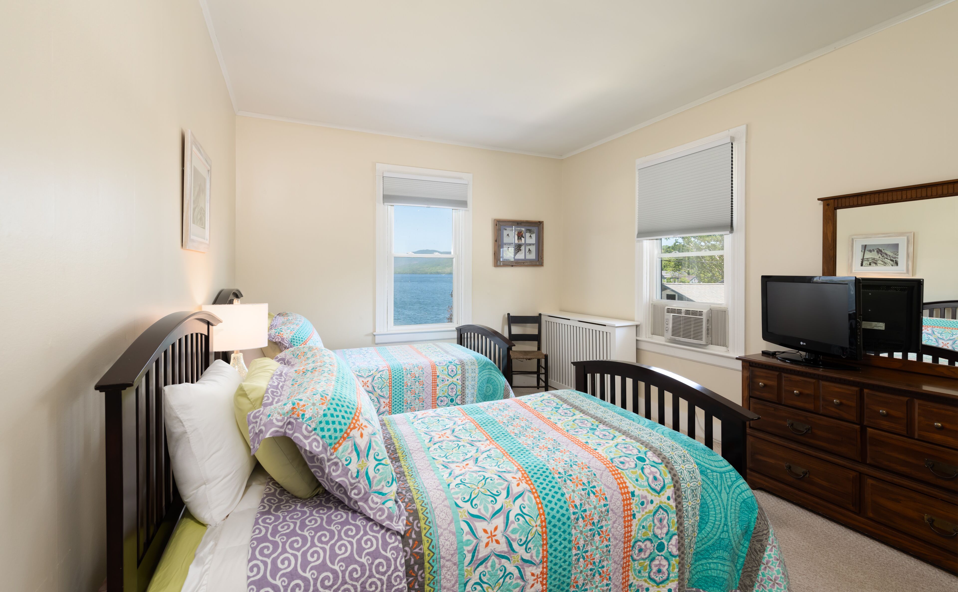 A bedroom with two beds, a dresser, a TV, and a window with a view of the water.