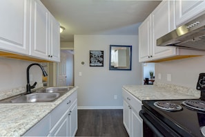 A kitchen with white cabinets, granite countertops, a black stove, and a stainless steel range hood.