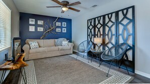 A living room with a beige sofa, two blue chairs, a ceiling fan, and a decorative wall panel. - 15 Mins to Closest Beach, 10 minutes from Downtown, with FIrepit! (Tampa)