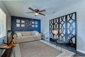 A living room with a beige sofa, two blue chairs, a ceiling fan, and a decorative wall panel.