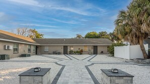 A building with a paved driveway leading to a gated entrance, surrounded by gravel and palm trees. - 15 Mins to Closest Beach, 10 minutes from Downtown, with FIrepit! (Tampa)