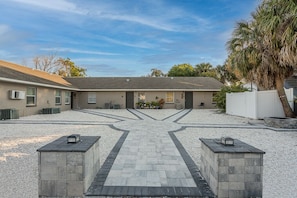A building with a paved driveway leading to a gated entrance, surrounded by gravel and palm trees.