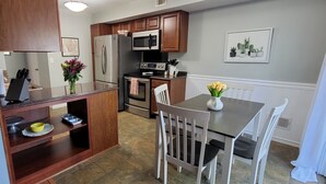 A kitchen with wooden cabinets, a refrigerator, a microwave, an oven, and a dining table with chairs.