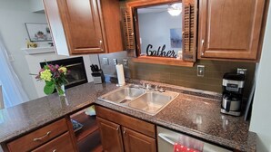 A kitchen with wooden cabinets, a double sink, a coffee maker, and a mirror with the word "Gather" on it.