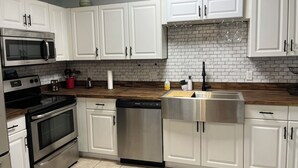 A modern kitchen with white cabinets, stainless steel appliances, a marble backsplash, and a wooden countertop. - Beautiful home in Oldsmar (Oldsmar)