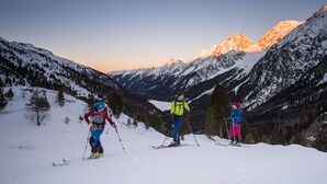 Trois skieurs sur une pente enneigée, avec un coucher de soleil en arrière-plan.
