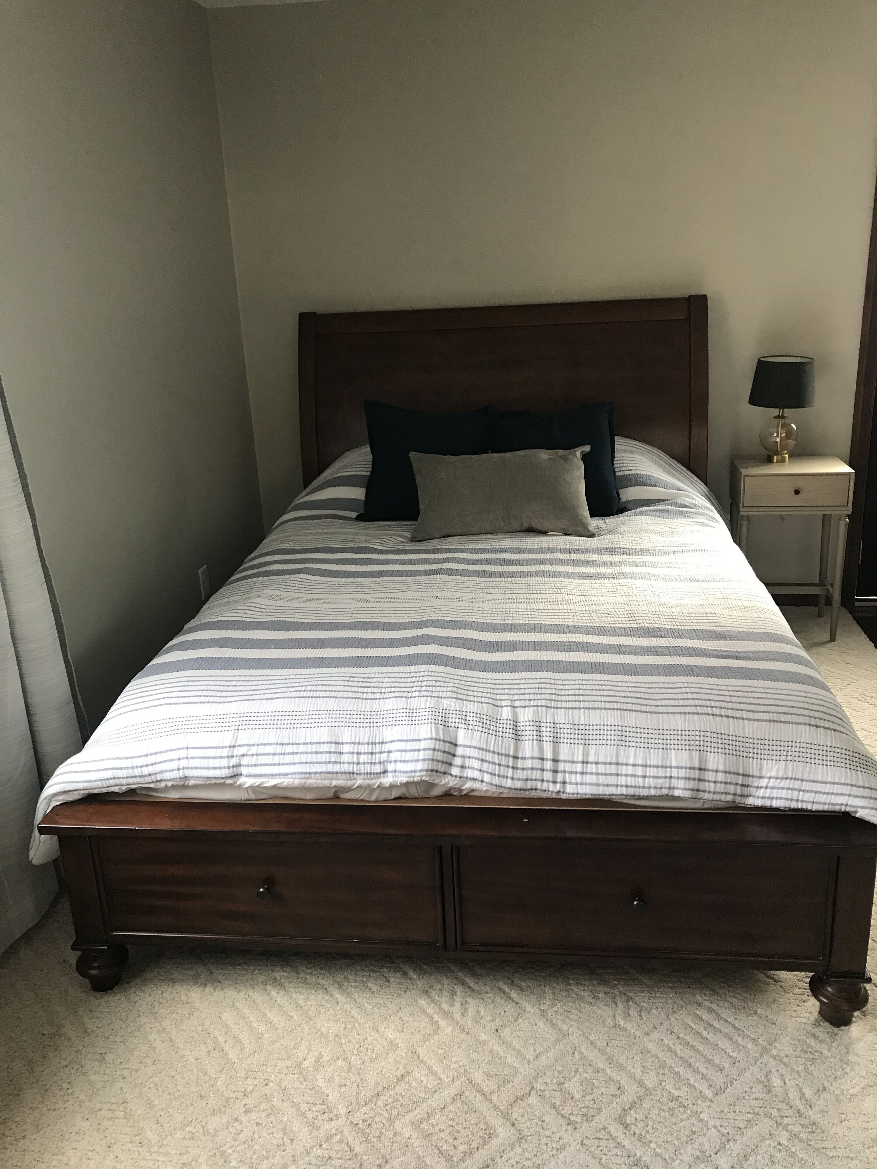 A single bed with a wooden headboard, a bedside table with a lamp, and a carpeted floor.