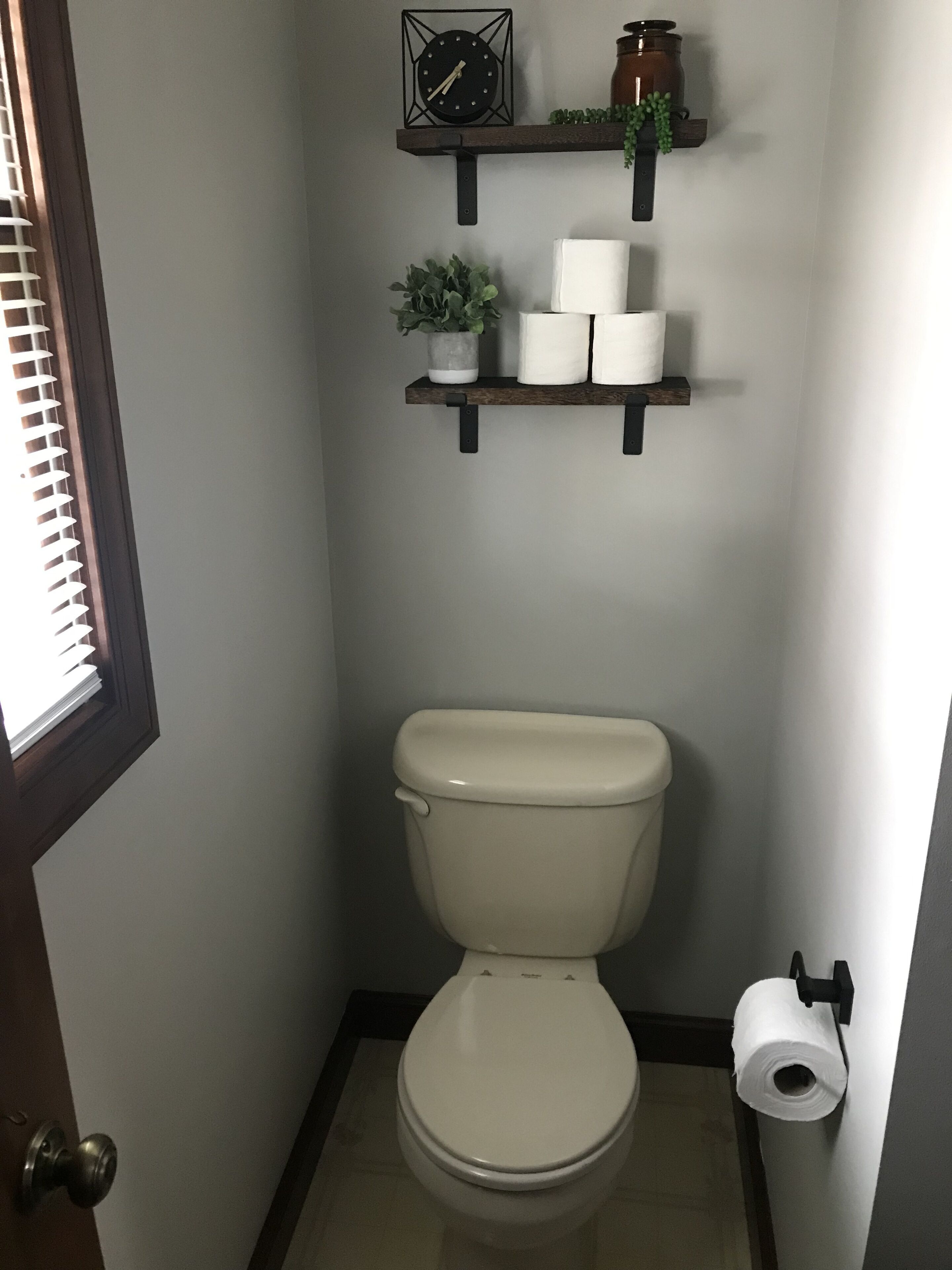 Ein Badezimmer mit Toilette, Ablagefläche mit Toilettenpapier und einer Uhr, sowie einer Zimmerpflanze.