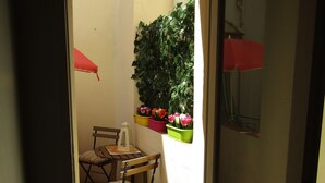 A small, enclosed balcony with a table and chairs, a potted plant, and a red umbrella.