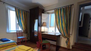 A room with two beds, a desk, a chair, and a window with curtains.