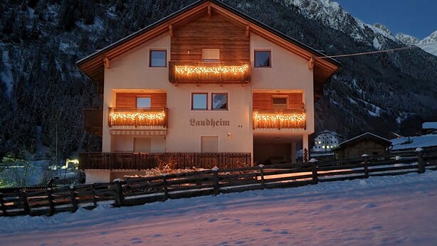 Un chalet de dos pisos con balcón, rodeado de montañas nevadas.