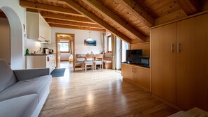 Un amplio salón con techo de madera, un sofá, una mesa de comedor con sillas y una zona de cocina con armarios y un televisor.