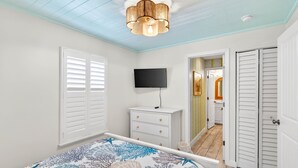 A bedroom with a bed, a TV, a dresser, and a hallway leading to another room. - Island Vibes House Steps from Clearwater Beach (Clearwater Beach)